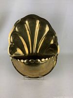 Front view of brass wall mounted plant holder showing shell shape design and scalloped bottom edge.