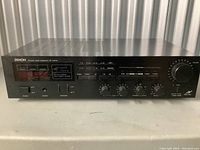Front view of black Denon AV receiver showing buttons, knobs, and digital display.