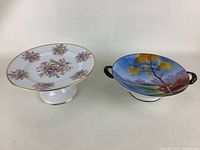 Two fine china pieces side by side showing floral pedestal compote and handled bowl with scenic painting