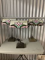 Group photo of three vintage Tiffany style table lamps with rectangular stained glass shades featuring floral patterns in pink, green, and white, and metal stepped square bases.