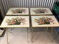 Four vintage folding TV tables arranged in a 2x2 grid showing rectangular tops with floral basket print and gold-toned thin metal legs.