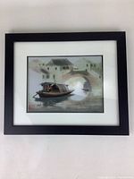 Framed small art on silk showing a traditional Asian boat scene with houses and a bridge, black wood frame, white matting, 12x10 inches approx.
