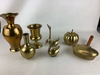 Seven vintage brass items arranged on white background: multiple vases, swan figurines, pumpkin container, and brass tray.