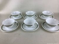 Six white teacups arranged with matching saucers, showing the set and pattern on each piece.