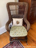 Front view of brown wicker rocking chair with floral seat cushion and embroidered back cushion