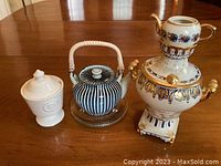 Overall view of the three items showing the Japanese teapot with striped design, Russian samovar, and sugar pot on a wooden table.