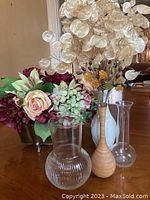 Multiple vases displayed with fabric and dried flowers in various materials and colors