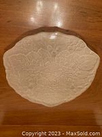 Top-down photo of clear beveled glass hot plate showing embossed floral and fruit pattern with scalloped edges.