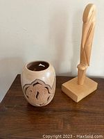 Photo showing light wood bird sculpture next to clay bowl with fish design.