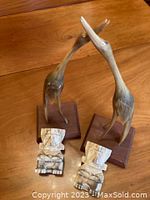 Two taller bird figurines on wooden bases with two smaller Mayan style carved bookends in front on a wood surface.