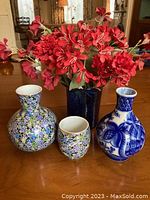 Set of four vases and red fabric flowers on a wooden table.