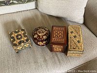 Four small wooden boxes with intricate inlay patterns arranged on a couch.