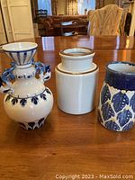 Photo showing three ceramic vases with different hand-painted designs on a wooden table.