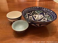 Three hand-crafted bowls grouped on a wood surface showing size and pattern variations