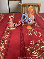 Photo of two hand-painted clay bird figurines, a rooster and a hen, on a red patterned tablecloth.