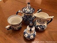 Teapot, milk jug, one tea cup and one doll-shaped sugar pot arranged on table