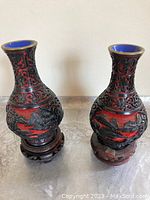 Photo showing a matched pair of decorative vases carved cinnabar over enamel on wooden stands, each about 6 inches tall with intricate red and black design