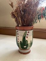 Single hand-painted Mexican-style ceramic vase with dried plants inside, showing green leaves and red berries design with terracotta accents on rim and base.