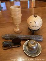 Overview of all objects on table including carved wooden goblet, spherical lantern with inscription, apple-shaped bowl with lid, carved wooden ruler, and two small sculptures.