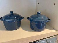 Photo shows two blue Cuisinart mini Dutch ovens with lids, each approximately one cup capacity, blue ceramic-coated cast iron, in good condition.
