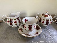 Set includes coffee pot, milk jug, sugar jug, cup and saucer showing the detailed red maple leaf and plaid designs with gold accent trim on porcelain.