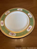 Top view of a Spaulding china dinner plate showing decorative green, gold, and floral border pattern.