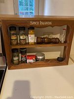 Front view of wooden Spice Islands branded two-shelf spice rack with various spices, grinders, and a sand timer.