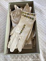 Photo of a box containing multiple pairs of vintage gloves in cream and beige colors, some with decorative buttons on cuffs, arranged flat