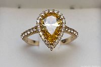 Front view of ring showing pear-shaped yellow center stone and halo on white jewelry box background