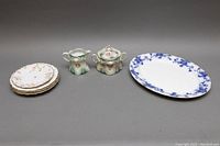 View of all items: flow blue platter, four Limoges plates stacked, Victoria Austrian creamer and sugar bowl