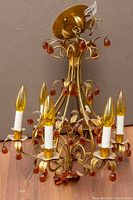 Full view of chandelier showing gilded scrolling frame, three faux-candle arms and amber glass teardrop pendants