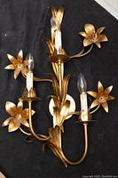 Front view of the 3-light floral gilded wall sconce showing cymbidium-style metal floral decorations around each light.