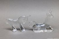 Front view of glass donkey and reclining unicorn paperweights side by side