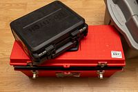 Closed black Bostitch drill case and closed red Contico toolbox stacked on wooden floor