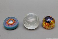 Three glass paperweights: blue floral millefiori, clear frosted swirl signed by Bertil Vallien, and multicolored floral dome.