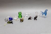 Wide shot of 12 small crystal and glass animal figurines arranged in a line showing variety of colors and shapes including green bear, blue horse, clear dogs.