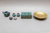 All six Chinese cloisonné enamel pieces arranged in a row with brass dish at right on neutral surface
