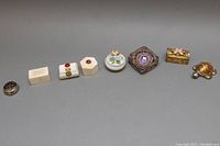 Wide view of all eight miniature trinket boxes in a line showing shape, size, and design differences.