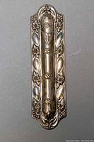 Front view of sterling silver repousse mezuzah case showing detailed floral and leaf relief work.