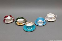 Five assorted porcelain teacup and saucer sets with varied colorful and gold detailed patterns shown from front angle.