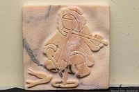 Close-up image of rosa aurora marble plaque with carved Inuit ice fisherman figure, showing color and veining of marble, and details of carving.