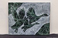 Front view of the Verdi marble plaque showing carved geese in flight against green and gray marble background.