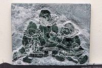 Full frontal image of the rectangular verdi marble plaque showing the carved and engraved depiction of three Inuit children in traditional attire, contrasting green and white marble tones.