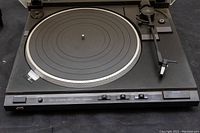 Front view of JVC turntable showing platter, tonearm, and control buttons.