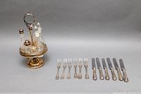 Photo showing full lot: 6-piece silver plated cruet set on revolving pedestal stand and 12-piece cutlery set with forks and knives in silver handles.
