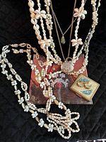 Overview photo displaying the five shell necklaces, two pendant necklaces, small pocket mirror, and earrings arranged on a black fabric background.