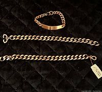Three vintage copper chain linked bracelets laid on black quilted surface. One smaller 8-inch bracelet with plate centerpiece and hook clasp. Two larger 9-inch bracelets with thick curb chain links and lobster claw clasps.