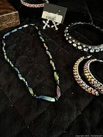 Full view showing black plastic rhinestone hoop earrings, black rhinestone cuff bracelet, hematite necklace, and cross earrings.
