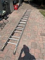 Full view of 25-foot aluminum extension ladder laid on paved ground, showing its length, rails, and rungs, with visible scratches and dents.