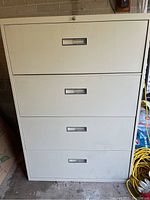 Metal filing cabinet with all four drawers closed, showing front exterior with recessed handles and beige finish.